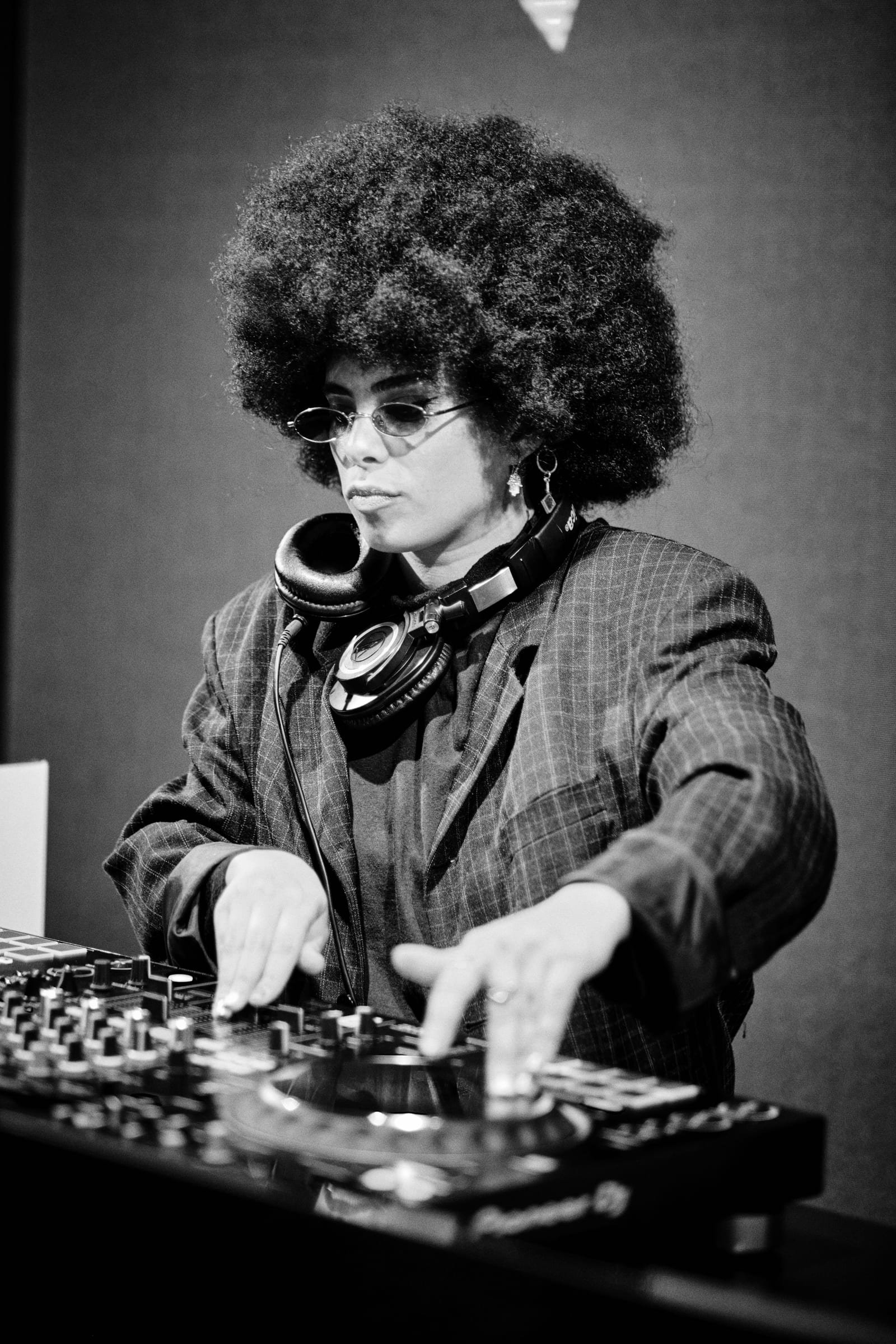 Allynx at the decks in black and white, headphones around the neck