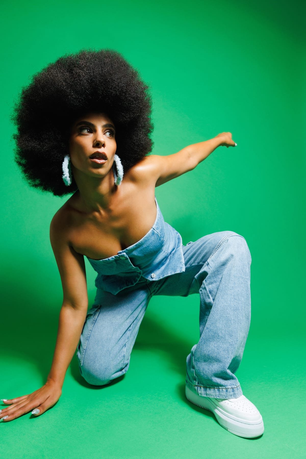 Allynx crouching low in a studio against a green backdrop, one arm extended.